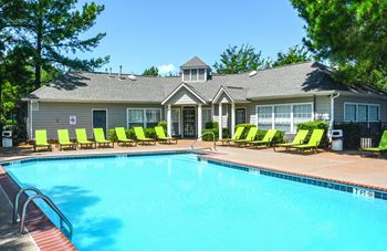 A pool with lounge chairs and a house in the background.